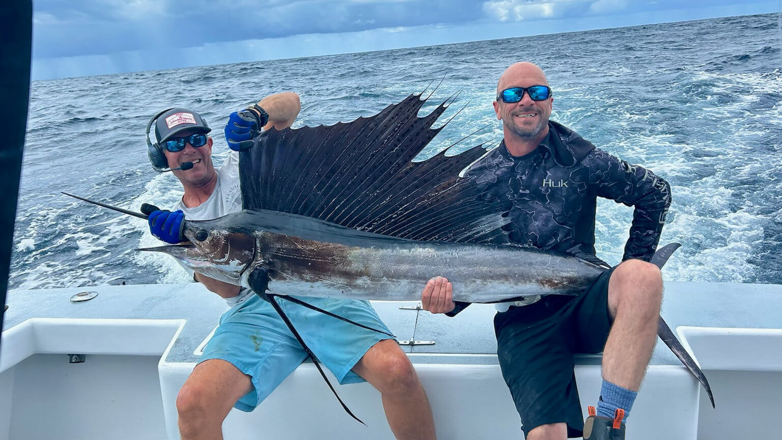 Mate helping a charter client Hold a sail fish at back of boat while offshore on a gulf steam charter